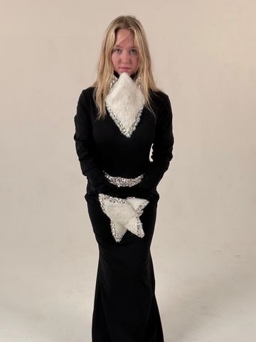 Woman in a black dress with white geometric embellishments posing against a plain background.