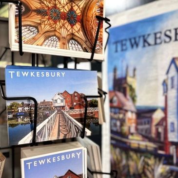 Postcards featuring Tewkesbury scenes displayed on a rack.
