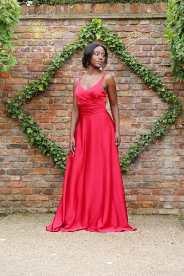 Woman in a red gown standing by a brick wall with ivy.