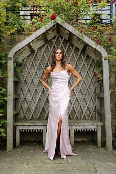 Woman in a pale pink gown standing in a garden alcove.
