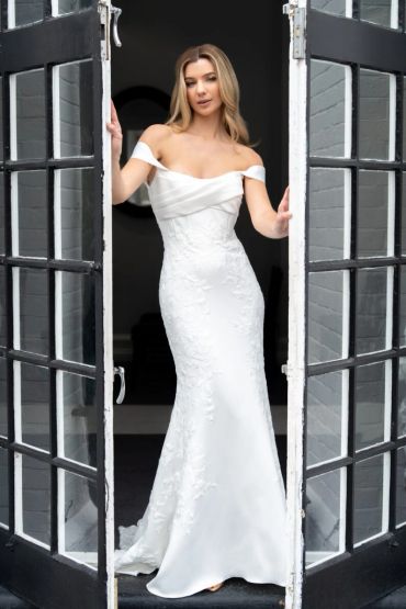 Woman in elegant white off-shoulder dress standing in a doorway.
