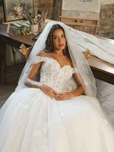 Bride in a white lace wedding dress sitting indoors.