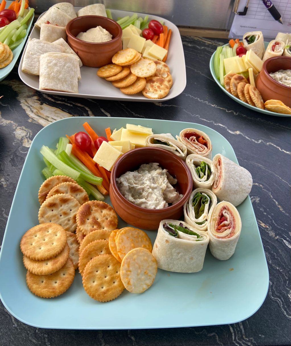 Plates with crackers, wraps, cheese, veggies, and dip.