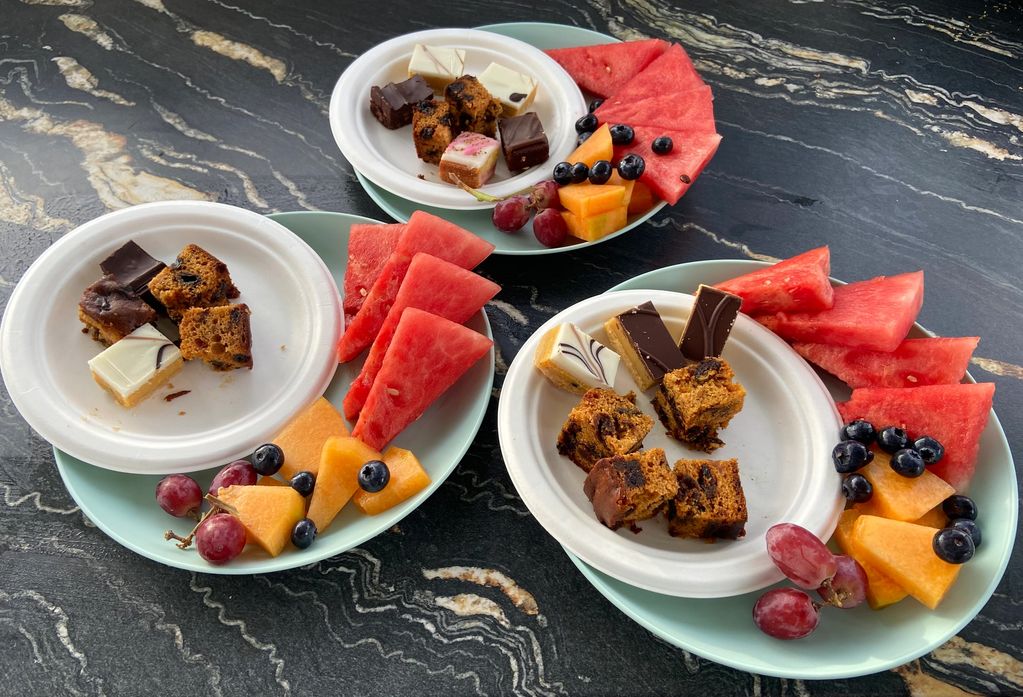 Plates with fruit and dessert bites on a marble table.