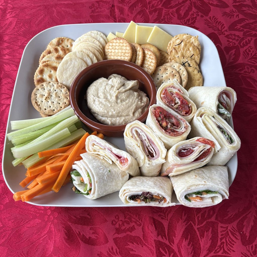 Platter with pinwheel wraps, crackers, veggies, and dip.