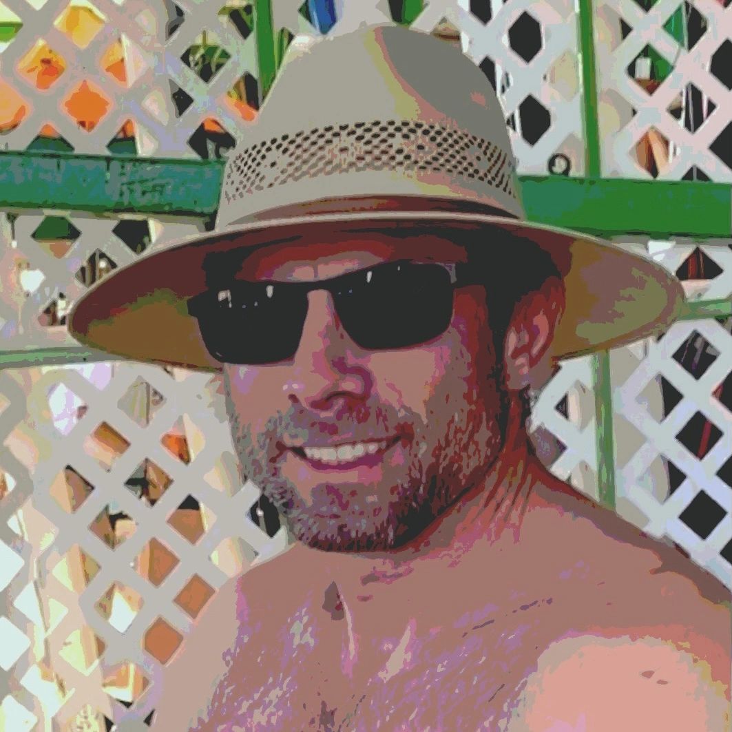 Smiling man wearing sunglasses and a straw hat against a lattice background.