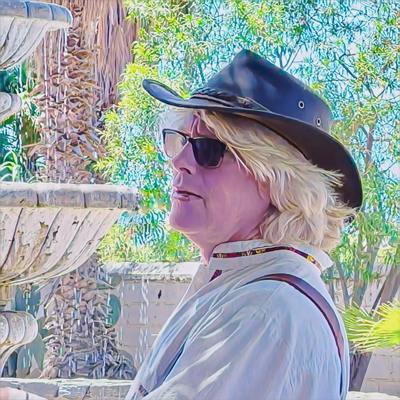 Woman in sunglasses and hat beside a stone fountain outdoors.