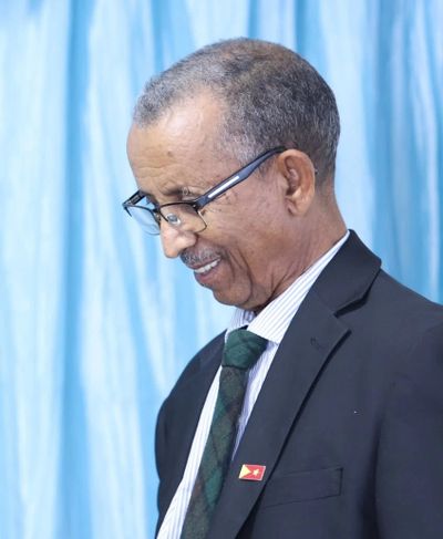 Elderly man in a suit and tie looking down with a smile.