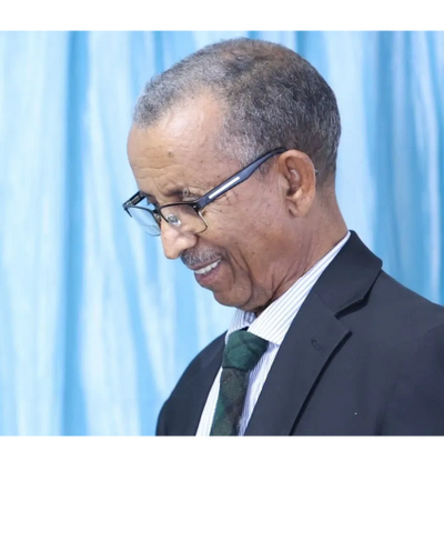 Smiling elderly man in glasses and suit against a blue curtain.