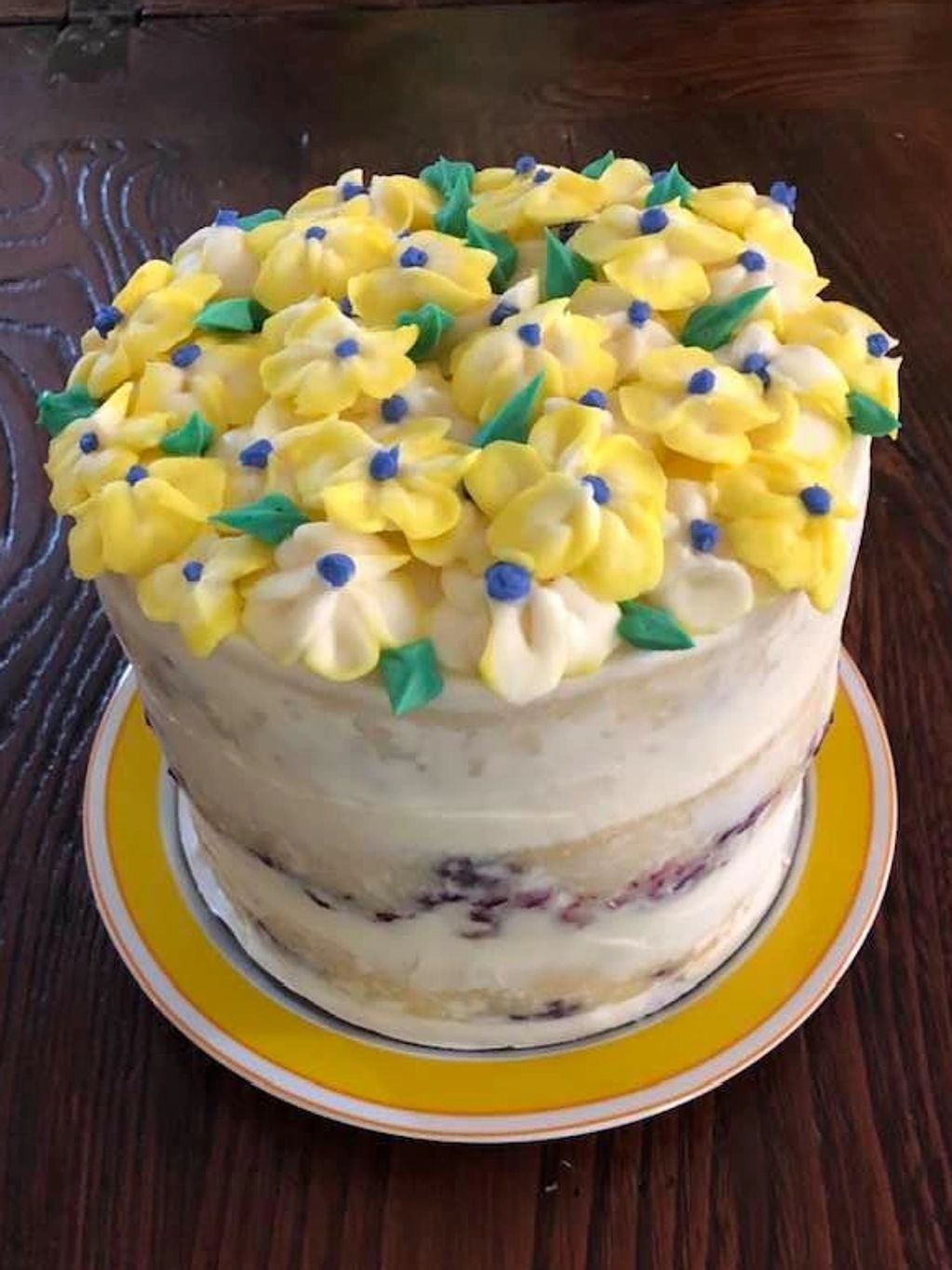 Six inch, three layer, lemon blueberry cake with naked frosting and buttercream flowers.