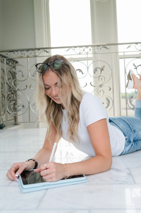 Woman lying on floor drawing on a tablet with a stylus.