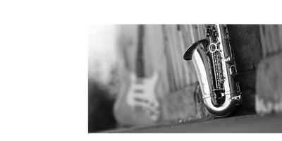 Black and white photo of a saxophone and a blurred guitar in the background.