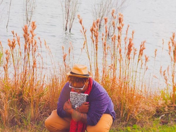 Person sitting by a lake with a notebook.