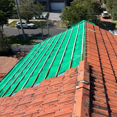 Roof renovation in progress with half tiled and half covered in green waterproofing.