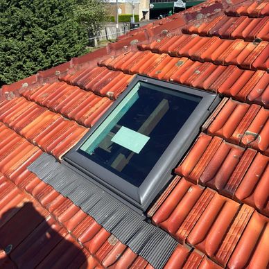 New skylight window installed on a red tiled roof under blue sky.
