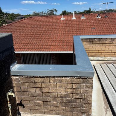 Brick wall with metal railing overlooking a red tiled roof under a clear blue sky.
