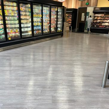 Supermarket aisle with frozen food section and a shopper.