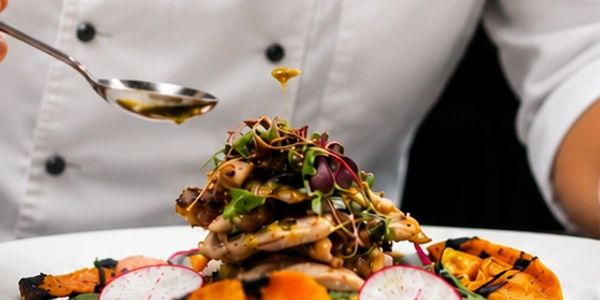 Chef drizzling sauce on a beautifully plated gourmet dish with vegetables.