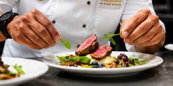 Chef garnishing a gourmet steak dish with fresh herbs.