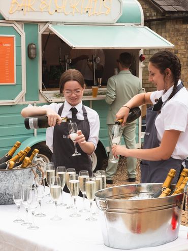 Two waitresses pouring champagne at an outdoor event.