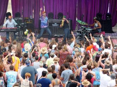 A lively band performs on stage with a crowd enjoying the music.