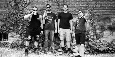 Four casually dressed men posing against a brick wall with vines.
