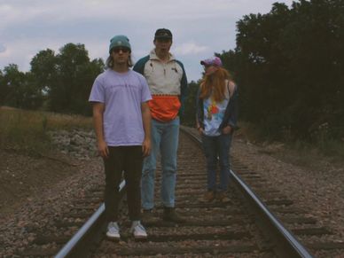 Three people standing on a railway track in casual attire.