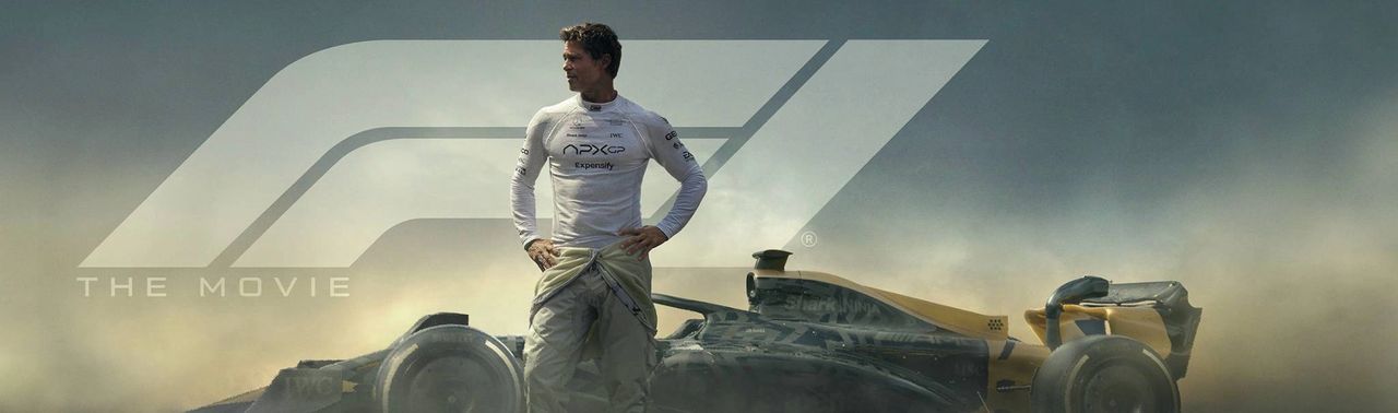 Brad Pitt in race gear standing next to the APX GP Formula 1 car with the F1 logo in the background, from the official promotional image for F1: The Movie.