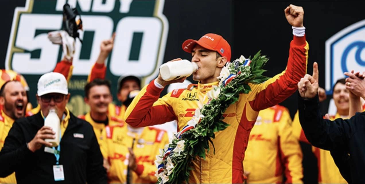 Alex Palou celebrates his 2025 Indianapolis 500 win on the podium, drinking milk in victory. Wearing his red and yellow DHL Chip Ganassi Racing suit and floral wreath, Palou becomes the first Spanish driver to win the Indy 500, surrounded by jubilant team members. Alex Palou celebrates his 2025 Indianapolis 500 win on the podium, drinking milk in victory. Wearing his red and yellow DHL Chip Ganassi Racing suit and floral wreath, Palou becomes the first Spanish driver to win the Indy 500, surrounded by jubilant team members.