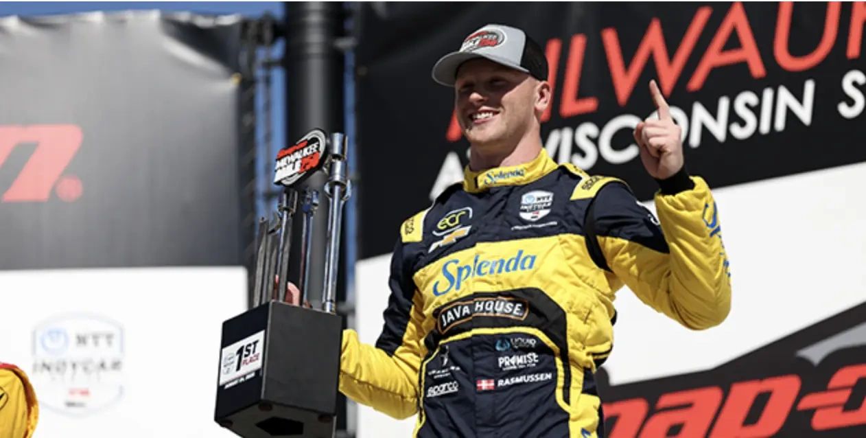 Christian Rasmussen celebrates Milwaukee Mile IndyCar win holding trophy in Ed Carpenter Racing suit