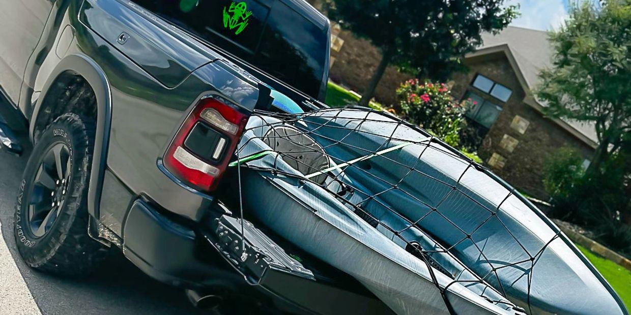Pickup truck carrying a kayak secured with a net.