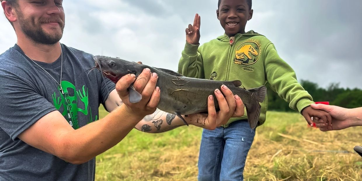 Man and boy holding a fish outdoors.