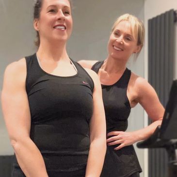 Two women in black workout attire smiling during a gym session.