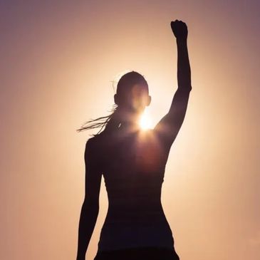 Silhouette of a person raising a fist against the sunset.
