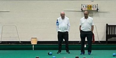 Two men at an indoor bowls club standing on the bowling green
