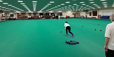 A woman bowling on an indoor bowls green