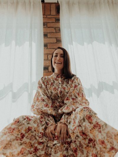 Sammy looking very happy, sitting in floral dress with brickwork and white curtains in the backgroun