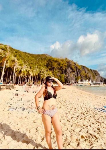 Woman in bikini enjoying sunny beach with palm trees and rocky hills.