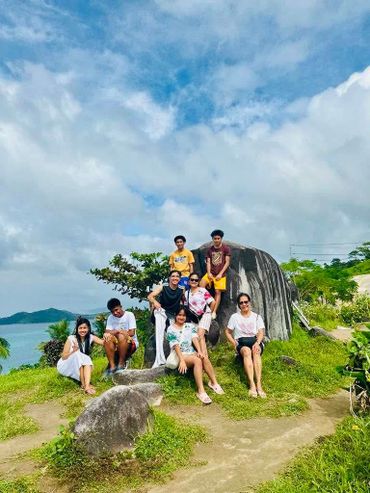 Group of friends posing on rocks with scenic ocean and sky background.
