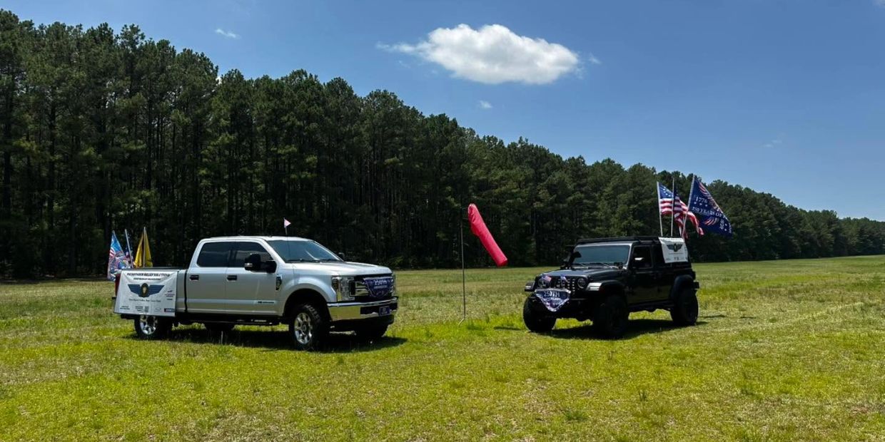 Two trucks parked on grass with flags on a sunny day.