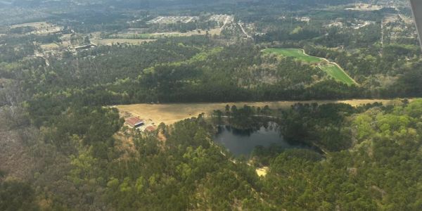 Aerial view of a forested area with a lake and scattered buildings.