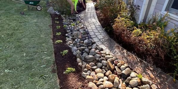 A person landscaping a garden with stones and plants along a curved pathway.