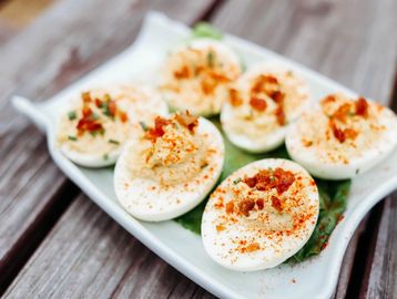 Plate of deviled eggs with paprika and bacon bits.