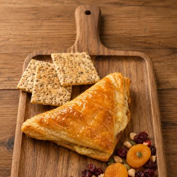 A triangular pastry with crackers and dried fruit on a wooden board.
