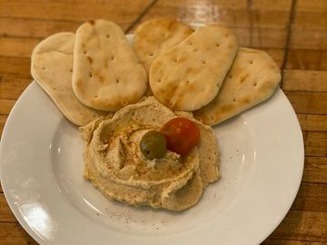 Hummus with pita chips, olive, and cherry tomato on a plate.