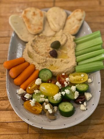 Plate with hummus, pita bread, celery, carrots, and Greek salad.
