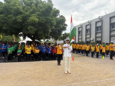 Student holding Indian flag at school event with groups in colored uniforms.