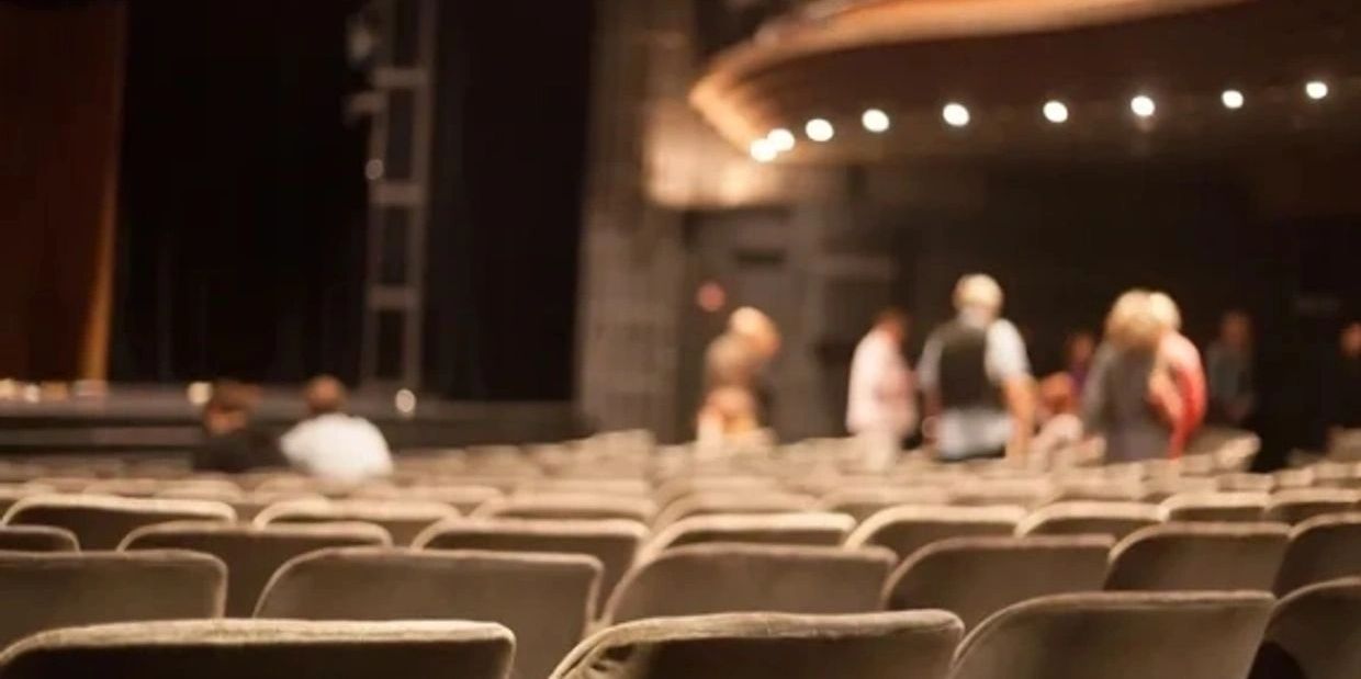 Empty theater seats with a few people standing in the background.