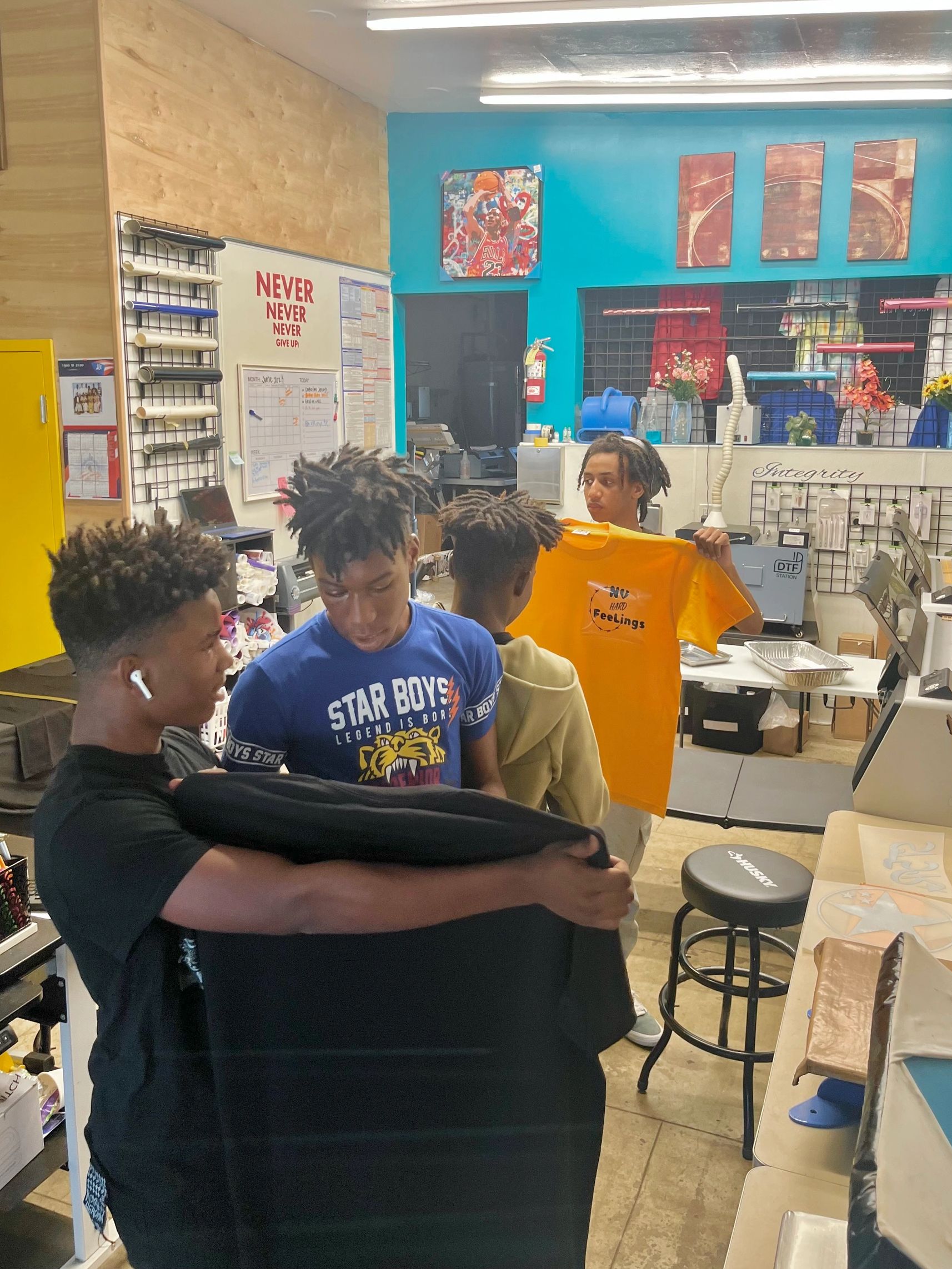 Four young men examining printed T-shirts inside a vibrant, organized workshop.