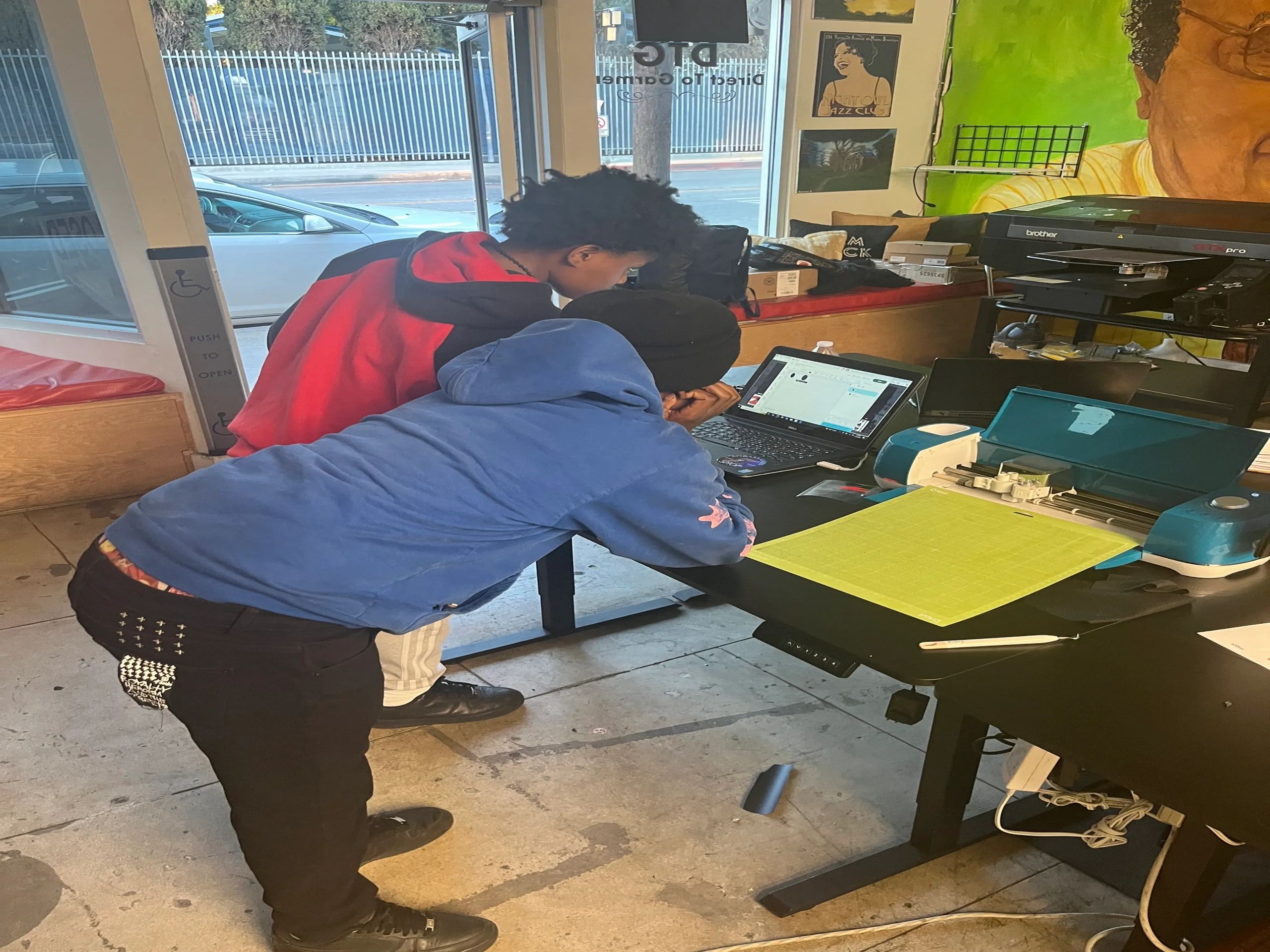 Two young people working together on a laptop in a workshop.
